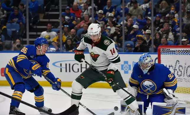 Minnesota Wild center Joel Eriksson Ek, center, stands over the puck as Buffalo Sabres center Noah Ostlund, left, and goalie Colten Ellis defend during the second period of an NHL hockey game Tuesday, Oct. 6, 2026, in Buffalo, N.Y. (AP Photo/Adrian Kraus)