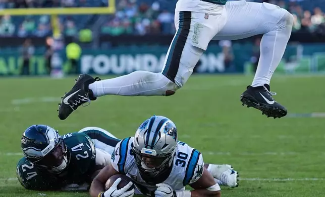 Carolina Panthers running back Chuba Hubbard (30) is brought down by Philadelphia Eagles safety Andrew Mukuba (24) as Eagles linebacker Zack Baun leaps during the second half of an NFL football game in Philadelphia, Sunday, Oct. 18, 2026. (AP Photo/Matt Rourke)