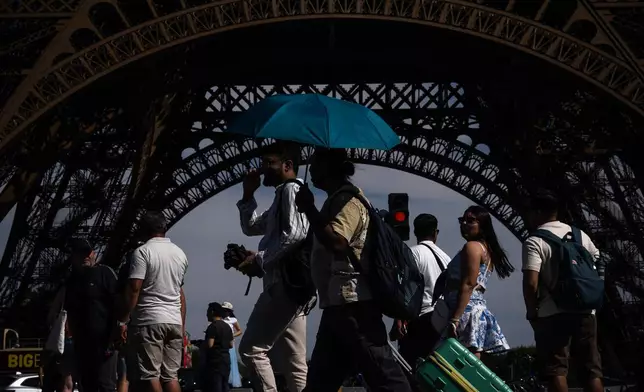 FILE - People walk with an umbrella near the Eiffel Tower in Paris during a heat wave July 11, 2026. (AP Photo/Aurelien Morissard, File)