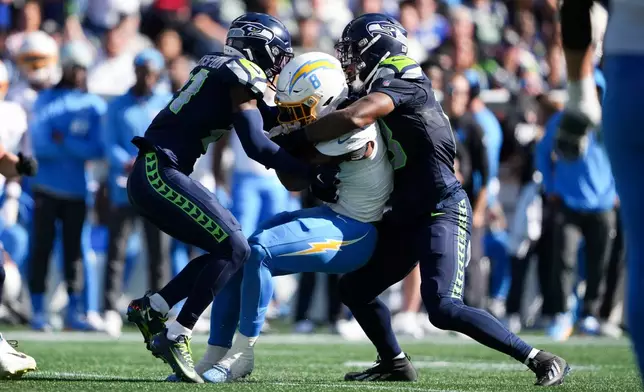 Los Angeles Chargers running back Omarion Hampton, center, is tackled by Seattle Seahawks cornerback Devon Witherspoon, left, and linebacker Ernest Jones IV, right, during the first half of an NFL football game, Sunday, Oct. 4, 2026, in Seattle. (AP Photo/Lindsey Wasson)