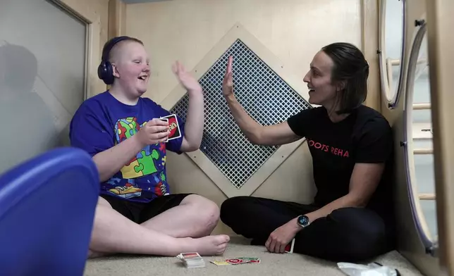 William Walter, 11, high fives his therapist, Charla Banks, at his occupational therapy appointment at Roots Rehab in Montana City, Mont., July 15, 2026. (AP Photo/Shelby Lum)
