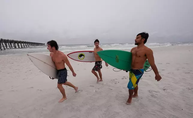 Surfers walk along the beach as Hurricane Isaias approaches Pensacola Beach, Fla., Friday, Oct. 9, 2026. (AP Photo/Gerald Herbert)