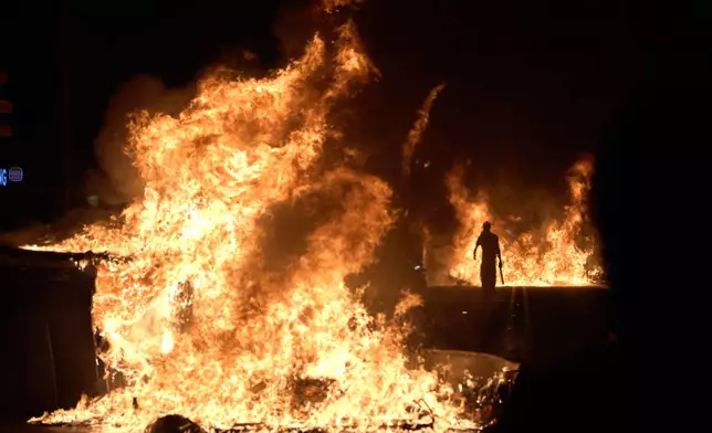 A demonstrator walks past burning trash cans set ablaze by protesters during clashes with police following a demonstration over Spain's housing crisis, hours after Prime Minister Pedro Sánchez announced an early general election, in Barcelona, Spain, Monday, Oct. 5, 2026. (AP Photo/Emilio Morenatti)