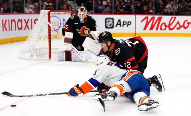Ottawa Senators' Thomas Chabot (72) slides on the ice with New York Islanders' Emil Heineman (51) as he tries to keep him from getting a shot on goaltender Linus Ullmark (35), during the first period of an NHL hockey game in Ottawa, Thursday, Oct. 15, 2026. (Justin Tang/The Canadian Press via AP)