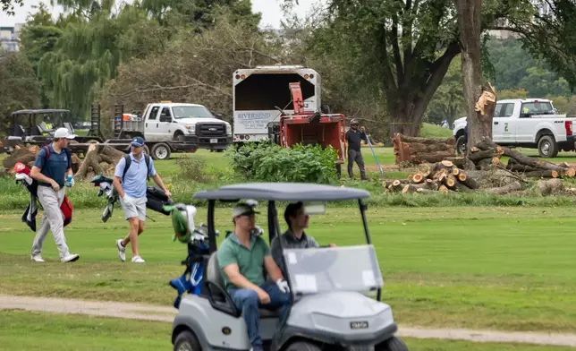 Golfers pass workers as the National Park Service begins cutting down trees at East Potomac Golf Links, Saturday, Oct. 10, 2026, in Washington. (AP Photo/Nathan Howard)