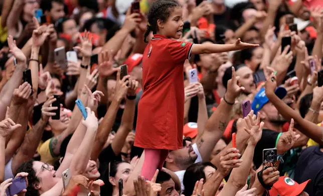 A girl standing on a man's shoulders reaches out amid a crowd of supporters of Brazilian President Luiz Inacio Lula da Silva, who is running for reelection, during his final campaign rally, a day ahead of the presidential runoff election in Sao Paulo, Brazil, Saturday, Oct. 24, 2026. (AP Photo/Natacha Pisarenko)