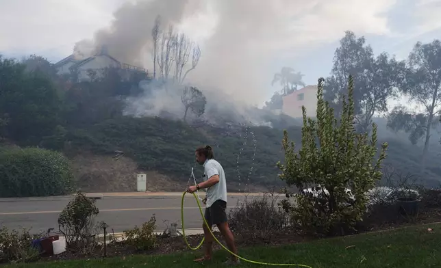 Resident Ephraim Taylor, grabs a garden hose in an effort to help with a wildfire spreading in his neighborhood, during the Norte Fire on Friday, Oct. 16, 2026, in San Juan Capistrano, Calif. (AP Photo/Jae C. Hong)