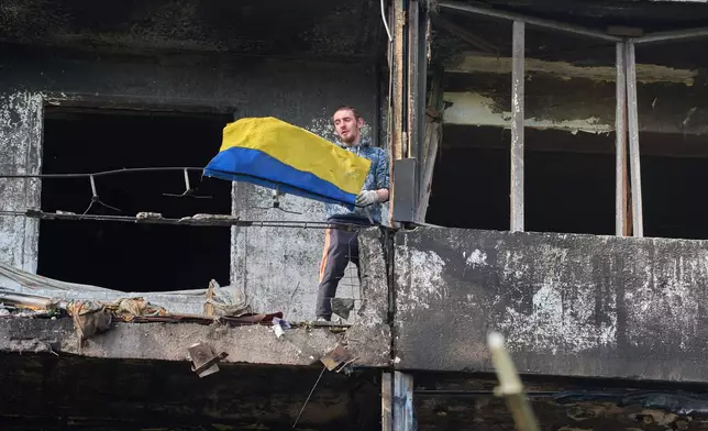 A man hangs out the national flag at his damaged apartment balcony after a missile strike during Russia's night air attack in Kyiv, Ukraine, Wednesday, Oct. 14, 2026. (AP Photo/Efrem Lukatsky)