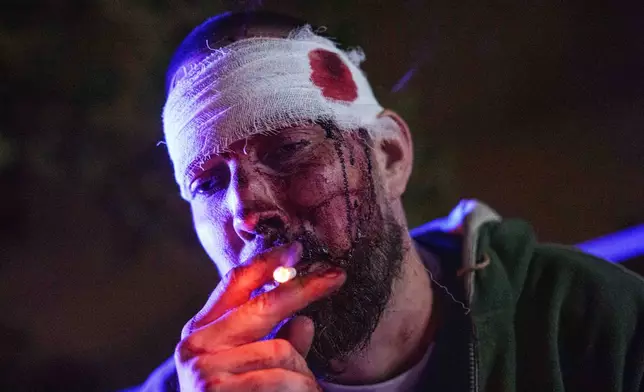 Andrii Parhomchuk, an injured resident, smokes a cigarette in front of his house damaged in a Russian missile strike in Kyiv, Ukraine, Wednesday, Oct. 14, 2026. (AP Photo/Evgeniy Maloletka)