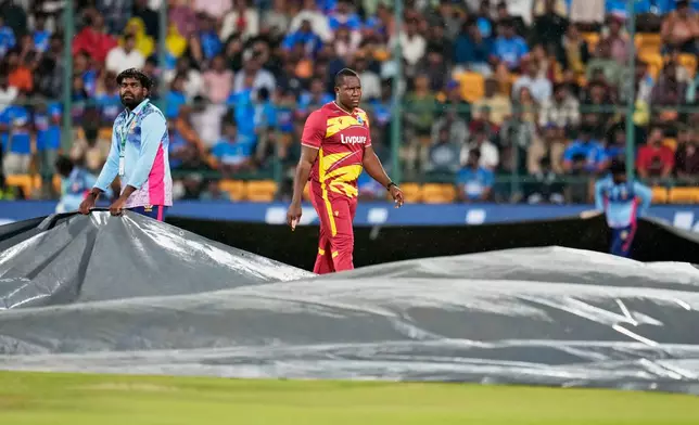 West Indies' Rovman Powell leaves the field as groundsmen cover the playing surface as rain disrupts play during the fifth T20 cricket match between India and West Indies in Bengaluru, India, Saturday, Oct. 17, 2026. (AP Photo/Aijaz Rahi)