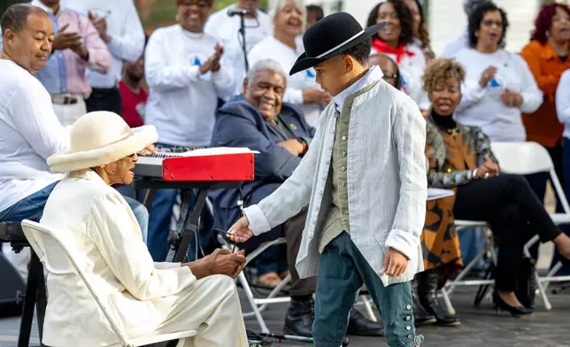 A child hands a slate pencil to church elder Mildred Taylor Walker, symbolizing the bond between generations and the ongoing fight for education, faith and freedom, during the rededication of the African Baptist Meeting House, now known as the First Baptist Church of Williamsburg, in Williamsburg, Va., Friday, Oct. 9, 2026. (AP Photo/Mike Kropf)