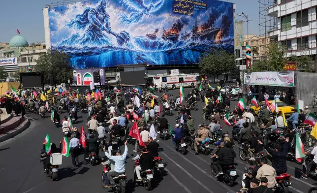 Motorcyclists drive past a billboard depicting a Persian legendary hero and flying figure hitting U.S. aircraft carriers alongside the message in English and Farsi: "From the Persian Gulf a new power rises" "The army of Satan will be drowned in the Persian Gulf, " during a state-organized motorcycle parade called "Janfada," meaning "Sacrifice for Iran,", in Tehran, Iran, Friday, Sept. 25, 2026. (AP Photo/Vahid Salemi)