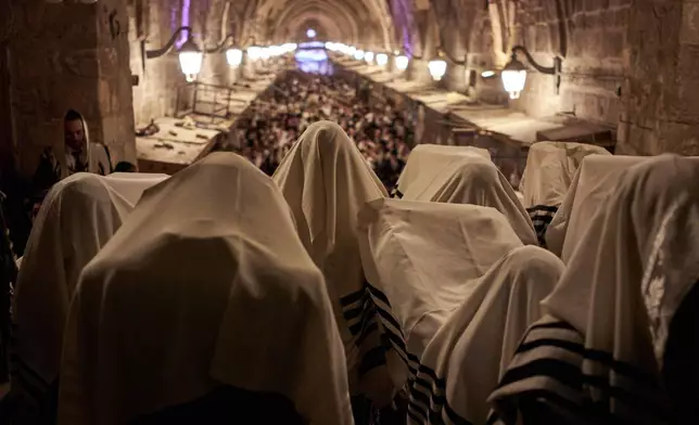 Covered in prayer shawls, Jewish men pray in front of the gate at Souq Al-Qattanin, or Cotton Merchants' Market, one of the entrances to the Al-Aqsa Mosque compound in the Old City of Jerusalem, Monday, Sept. 28, 2026, during morning prayers for the Jewish holiday of Sukkot. (AP Photo/Leo Correa)