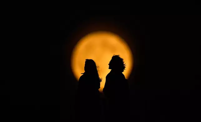 The full moon rises behind the silhouettes of people walking in Istanbul, Turkey, Saturday, Sept. 26, 2026. (AP Photo/Emrah Gurel)