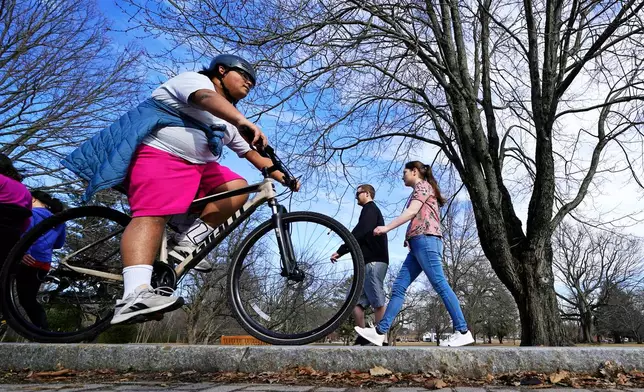 FILE - A bike rider in shorts rolls past a couple walking at the town common in North Andover, Mass., Feb. 23, 2022. (AP Photo/Charles Krupa, File)
