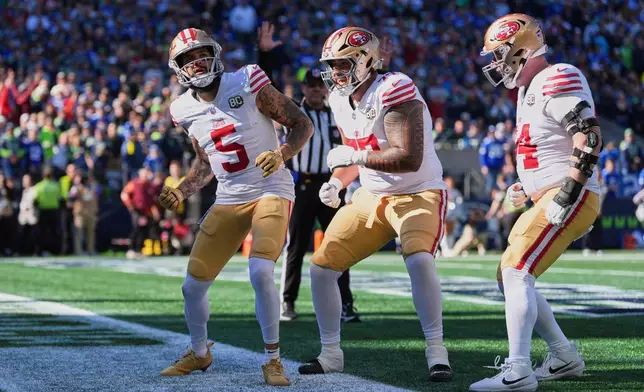 San Francisco 49ers wide receiver Mike Evans (5) celebrates his touchdown catch with offensive tackle Dominick Puni (77), and enter Jake Brendel (64) during the first half of an NFL football game against the Seattle Seahawks, Sunday, Oct. 11, 2026, in Seattle. (AP Photo/Lindsey Wasson)