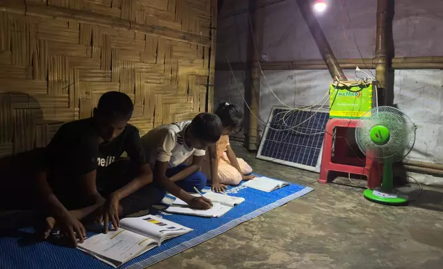 In this photo taken with a phone, children use a light powered by a solar panel to study at night inside their shelter on Oct. 3, 2026, in Teknaf, Bangaldesh. (AP Photo/Abdul Khan Dkl)