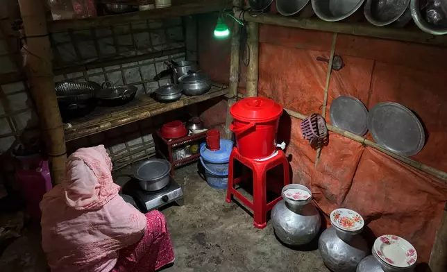In this photo taken with a phone, a woman uses a light powered by solar panels in her kitchen on Oct. 4, 2026, in Teknaf, Bangaldesh. (AP Photo/Abdul Khan Dkl)