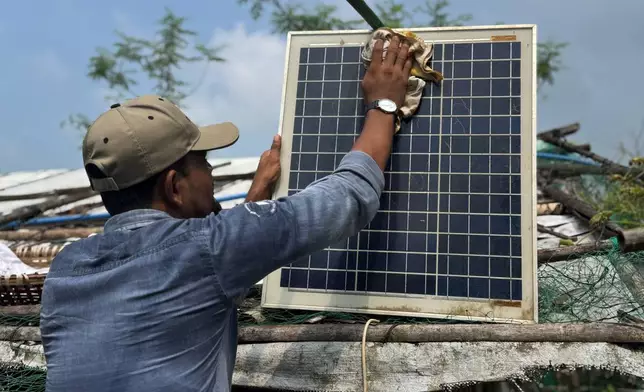 In this photo taken with a phone, Mohammed Saber cleans a solar panel to ensure it charges properly on Oct. 4, 2026, in Teknaf, Bangaldesh. (AP Photo/Abdul Khan Dkl)