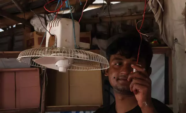 In this photo taken with a phone, Mohammed Hares turns on a solar-powered fan inside his shop Oct. 4, 2026, in Teknaf, Bangaldesh. (AP Photo/Abdul Khan Dkl)