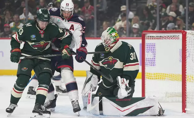 Minnesota Wild goaltender Jesper Wallstedt (30) and defenseman Quinn Hughes (43) defend against a shot as Columbus Blue Jackets center Sean Monahan (23) pressures them during the first period of an NHL hockey game, Sunday, Oct. 18, 2026, in St. Paul, Minn. (AP Photo/Abbie Parr)