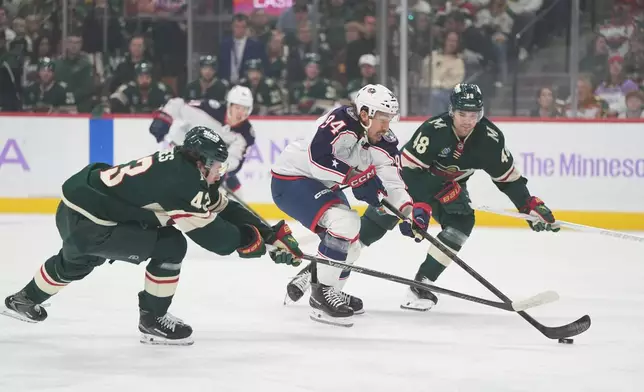 Columbus Blue Jackets left wing Ryan Lomberg (94) skates with the puck as Minnesota Wild defensemen Quinn Hughes, left, and Daemon Hunt, right, defend during the first period of an NHL hockey game, Sunday, Oct. 18, 2026, in St. Paul, Minn. (AP Photo/Abbie Parr)
