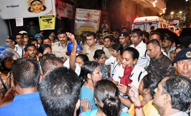 People gather outside as police officers set up a barricade at the entrance to a worship venue for the Hindu festival of Durga Puja following a stampede, in Kolkata, India, Saturday, Oct. 17, 2026. (AP Photo)