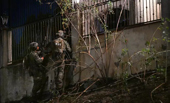 Federal agents stand outside a suspect's house during a raid related to health care fraud in the early morning on Thursday, Oct. 22, 2026, in Los Angeles. (AP Photo/Wally Skalij)
