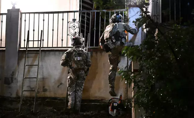 Federal agents climb a fence to enter a suspect's house during a raid related to health care fraud in the early morning on Thursday, Oct. 22, 2026, in Los Angeles. (AP Photo/Wally Skalij)