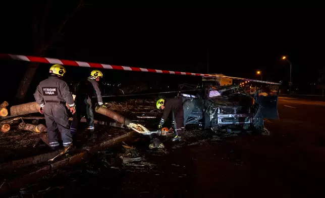 Emergency workers clear debris and damaged road infrastructure near a destroyed car following a Russian overnight strike in Kyiv, Ukraine, Tuesday, Oct. 27, 2026. (AP Photo/Dan Bashakov)