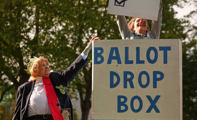 Dressed as President Donald Trump, Victoria Millard, left, tries to stop Jessica Jones, right, from putting a ballot in a drop box during a skit by 350 Seattle and the Troublemakers at the end of the "No Kings" protest march encouraging early voting Saturday, Oct. 17, 2026, in Seattle. (AP Photo/Lindsey Wasson)