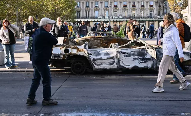 People look at a charred car on Place de la Republique the day after a demonstration against rising living costs, joining students' grievances, in Paris, Sunday, Oct. 18, 2026. (AP Photo/Emma Da Silva)