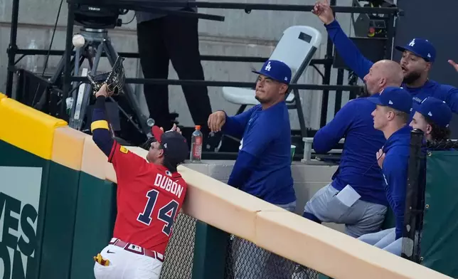 Atlanta Braves left fielder Mauricio Dubón (14) climbs the wall to catch a fly out by Los Angeles Dodgers' Freddie Freeman as the Dodgers bullpen look on during the third inning in Game 3 of baseball's National League Division Series, Tuesday, Oct. 6, 2026, in Atlanta. (AP Photo/Mike Stewart)