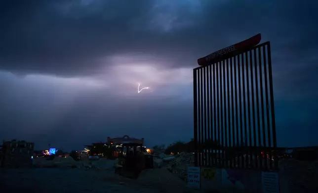 Lightning illuminates the sky behind a mockup of the border wall in protest of proposed barriers along the border, Thursday, Sept. 24, 2026, in Terlingua, Texas. (AP Photo/John Locher)