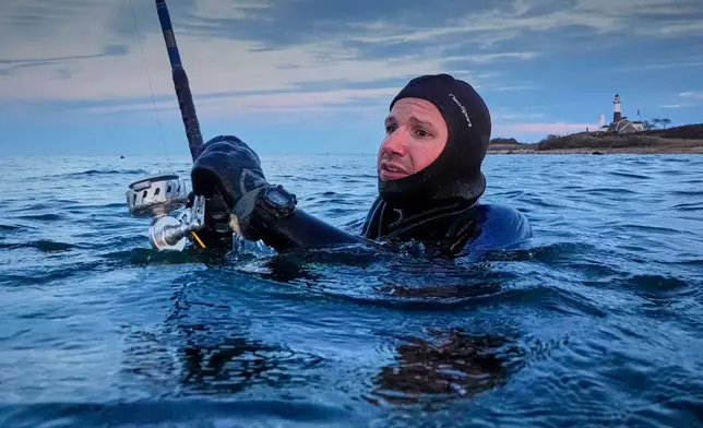 Jason Markowitz wears a wetsuit in the chilly water off Montauk Point while fishing for striped bass, Saturday, Oct. 10, 2026, in Montauk, N.Y. (AP Photo/Robert F. Bukaty)