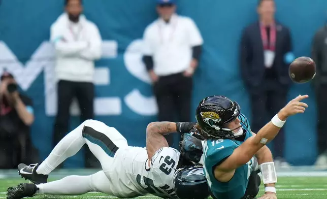 Jacksonville Jaguars quarterback Trevor Lawrence (16) passes as he's tackled by Philadelphia Eagles linebacker Zack Baun (53) during an NFL football game in London, Sunday, Oct. 11, 2026. (AP Photo/Alastair Grant)