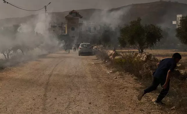 A Palestinian youth runs from tear gas fired by members of Israeli forces following a settler attack during the olives harvest in the West Bank village of Abu Falah, Friday, Oct. 16, 2026. (AP Photo/Leo Correa)