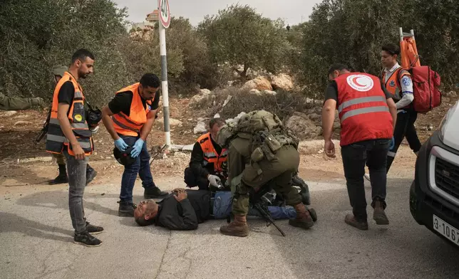 Palestinian medics and an Israeli soldier attend to a Palestinian man shot by Israeli soldiers following a settler attack on Palestinians harvesting olives in the West Bank village of Abu Falah, Friday, Oct. 16, 2026. (AP Photo/Leo Correa)