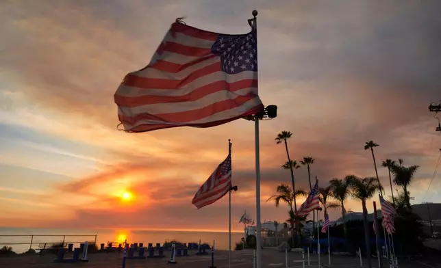 FILE - Flags fly under heavy winds before sunset as a plume of smoke from the Franklin Fire rises over the ocean Tuesday, Dec. 10, 2024, in Malibu, Calif. (AP Photo/Damian Dovarganes,File)