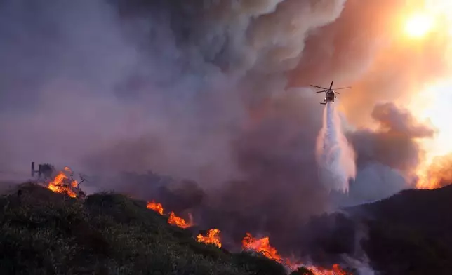 FILE - Water is dropped by helicopter on the advancing Palisades Fire in the Pacific Palisades neighborhood of Los Angeles, Jan. 7, 2025. (AP Photo/Etienne Laurent, File)