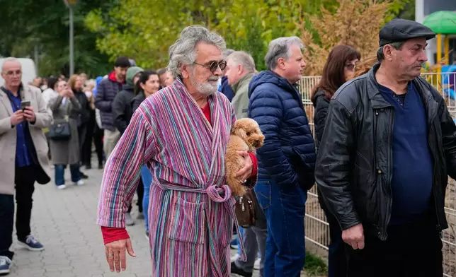 A man holds a dog while arriving at a polling station to vote in a parliamentary election in Belgrade, Serbia, Sunday, Oct. 25, 2026. (AP Photo/Petr David Josek)