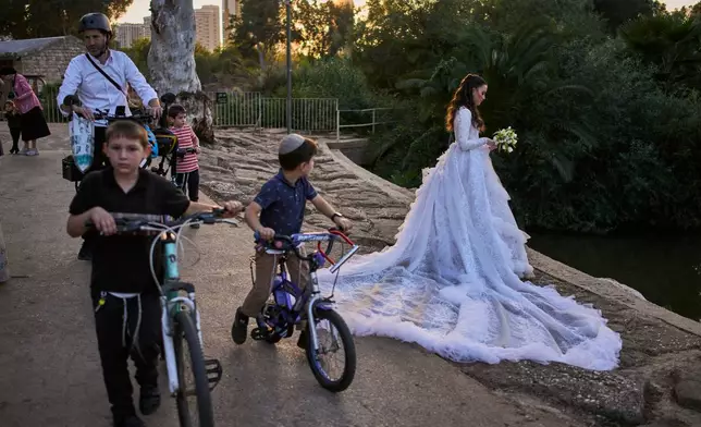 People ride their bicycles past a bride posing for a photoshoot on her wedding day at Hayarkon Park in Tel Aviv, Israel, Wednesday, Oct. 28, 2026. (AP Photo/Oded Balilty)