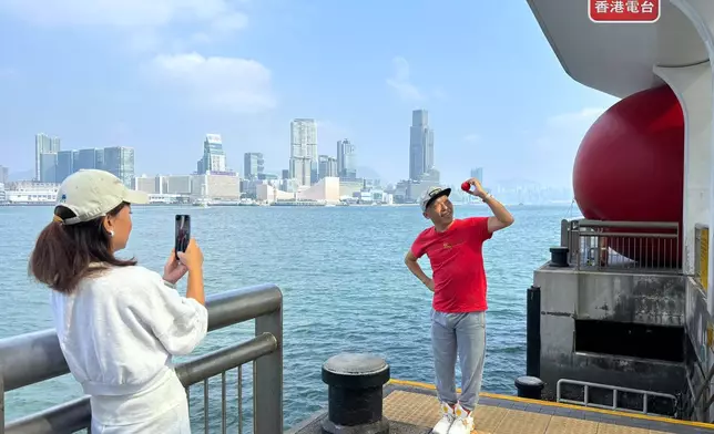 有人身穿紅色上衣手持小紅球與藝術品「紅球」合照。