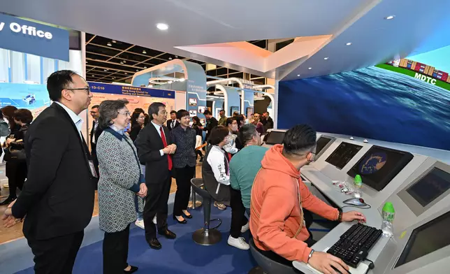 楊何蓓茵（左二）及公務員事務局常任秘書長梁卓文（左三）在海事處的攤位觀看全功能船舶模擬器的示範。 政府新聞處圖片