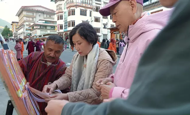 二人在不丹旅遊達人帶領下閒逛諾辛蘭大道，並購買節慶才發售的彩票。