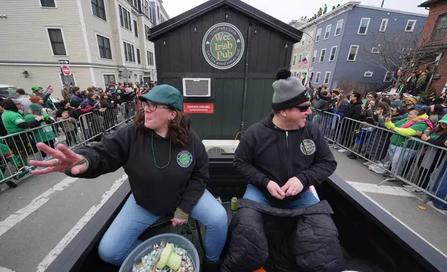 迪娜泰勒（Dena Taylor，左）和東尼迪多納托（Tony DiDonato）乘坐一輛拖着「小愛爾蘭酒吧」（The Wee Irish Pub）的卡車，向觀眾拋擲糖果。這間功能齊全的流動愛爾蘭酒吧由麻省兩兄弟建造，攝於2026年3月15日（周日）南波士頓（South Boston）社區舉行的年度聖派翠克節巡遊期間。(美聯社圖片/Charles Krupa) AP圖片
