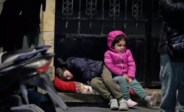 2026年3月2日週一清晨，黎巴嫩南部港口城市賽達，從黎巴嫩南部逃離以色列空襲的流離失所家庭抵達，兒童坐在人行道上。(美聯社圖片/Mohammed Zaatari) AP圖片