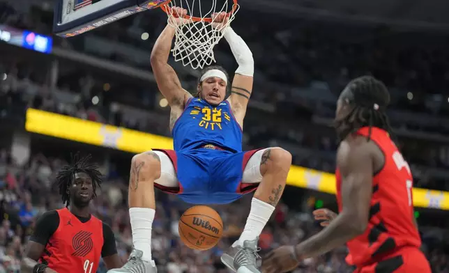 丹佛金塊前鋒艾朗哥頓（Aaron Gordon）（中）在周日（2026年3月22日）於丹佛舉行的一場NBA籃球賽下半場，在波特蘭拓荒者後衛施索高（Sidy Cissoko）（左）及賀列特（Jrue Holiday）之間入樽得分後掛在籃框上。 (美聯社圖片/David Zalubowski) AP圖片