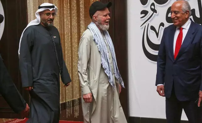 美國阿富汗問題特別代表扎爾邁哈利勒扎德（右）及阿拉伯聯合酋長國駐喀布爾大使賽義夫阿爾凱特比（左）陪同下，美國公民丹尼斯科伊爾（中）在喀布爾機場登機前微笑。AP圖片