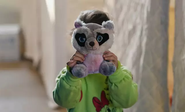 2026年3月10日周二，黎巴嫩貝魯特，一名流離失所的女孩在卡米勒夏蒙體育城體育場內，用毛絨玩具遮住臉部躲避攝影師。該體育場已改建為收容中心，安置因以色列空襲黎巴嫩南部及貝魯特南郊達希耶而逃難的民眾。(美聯社圖片/Hassan Ammar) AP圖片